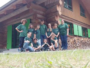 Gruppe der Kinder und Betreuenden steht in grünen T-Shirts vor der Wildnisstation